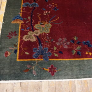 Red rug featuring a detailed floral pattern and a dark green border rests on distressed blonde wood planks.