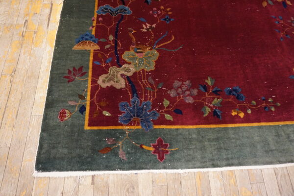 Red rug featuring a detailed floral pattern and a dark green border rests on distressed blonde wood planks.