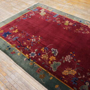 A burgundy rug featuring a floral vine pattern and wide green border sits on distressed wood flooring.