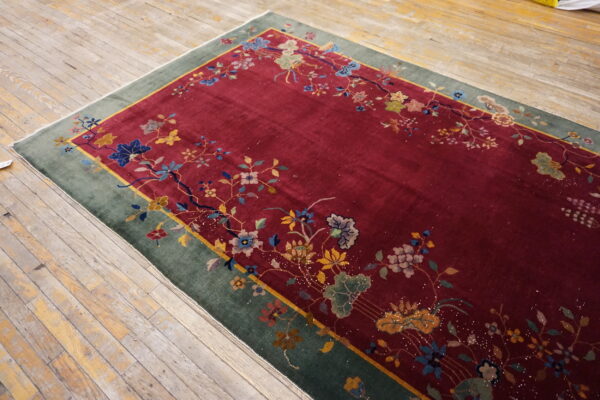A burgundy rug featuring a floral vine pattern and wide green border sits on distressed wood flooring.