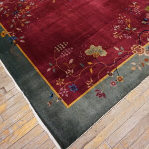 Deep red rug with multicolor floral vines and a green border lies on worn light wood flooring.