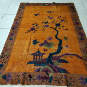 Orange rug with a scenic pagoda and flowering tree pattern in blue and purple colors on white tile.