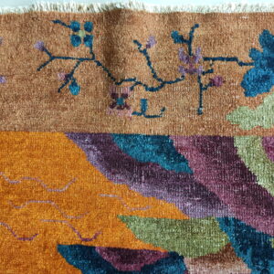 Close-up showing multicolored rug pile with rust, orange, blue, and purple floral and abstract patterns.