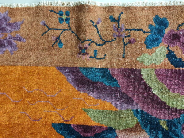 Close-up showing multicolored rug pile with rust, orange, blue, and purple floral and abstract patterns.