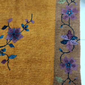 Golden yellow high-pile rug with stylized purple and blue flowers and a contrasting brown floral border.