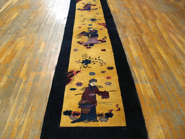 Gold runner rug with black borders and repeating figural motifs laid across worn wooden plank flooring.