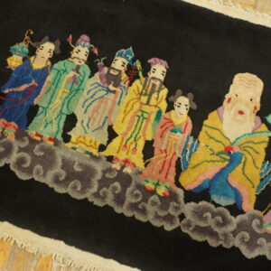 A black rug with multicolored figures standing on gray clouds lies on distressed yellow wood floor.
