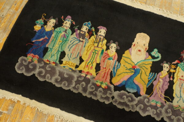A black rug with multicolored figures standing on gray clouds lies on distressed yellow wood floor.