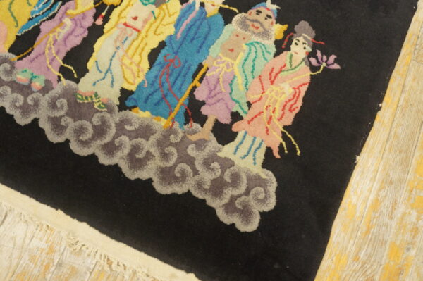 A high-pile black rug features a brightly colored pattern of figures on clouds over worn wood floors.