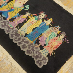 Black rug with a brightly colored figural pattern resting on distressed light wood flooring.