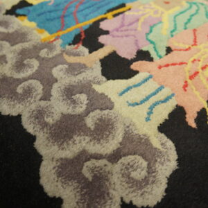 A medium pile rug has a black field with colorful abstract and cloud motifs in pastel and gray tones.