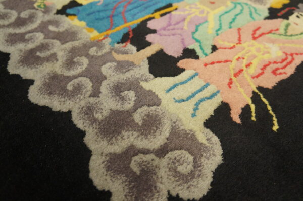 A medium pile rug has a black field with colorful abstract and cloud motifs in pastel and gray tones.