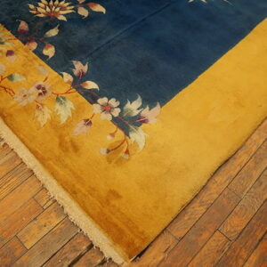 Deep blue rug field bordered by gold, featuring pale floral vine patterns on plank wood flooring.