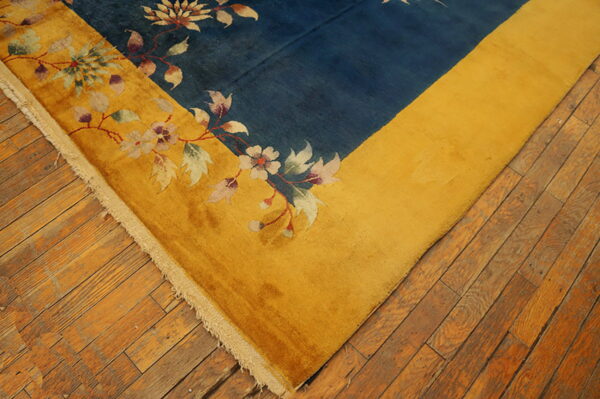 Deep blue rug field bordered by gold, featuring pale floral vine patterns on plank wood flooring.