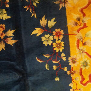 Detail of a dark blue rug with a yellow border and red, orange, and pale green floral designs.