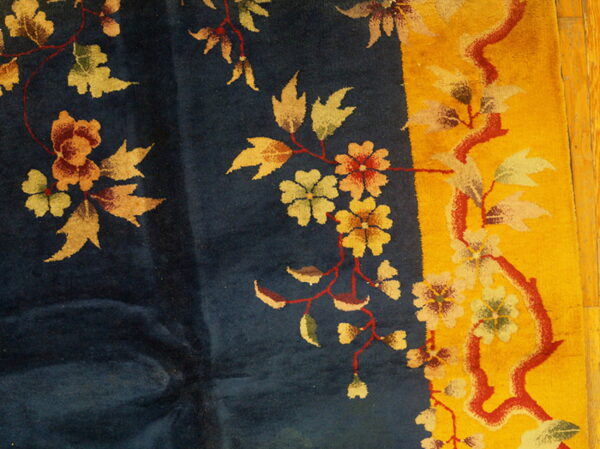 Detail of a dark blue rug with a yellow border and red, orange, and pale green floral designs.