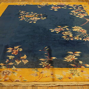 Oversized navy rug with a wide gold border features scattered floral and vine designs on wood planks.