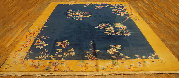 Oversized navy rug with a wide gold border features scattered floral and vine designs on wood planks.