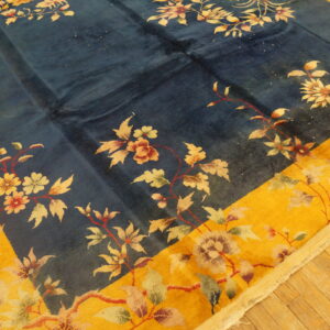 Blue field rug with a bold yellow border and floral pattern on diagonal wood plank flooring.