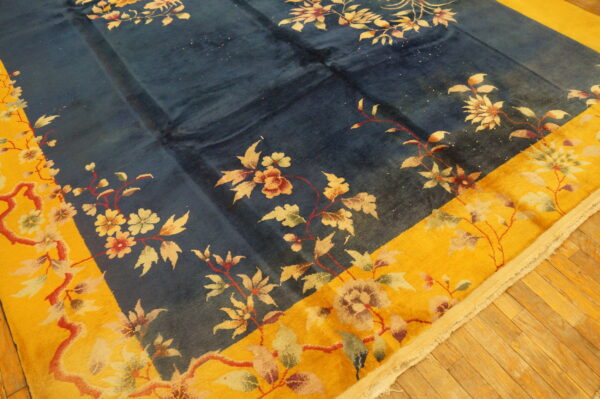 Blue field rug with a bold yellow border and floral pattern on diagonal wood plank flooring.