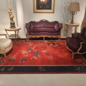 Ornate red rug with flowering branches and a navy border anchors a room with gilded furniture.