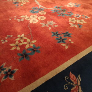 Red floral rug with blue and cream blossoms bordered by dark navy featuring a visible butterfly motif.