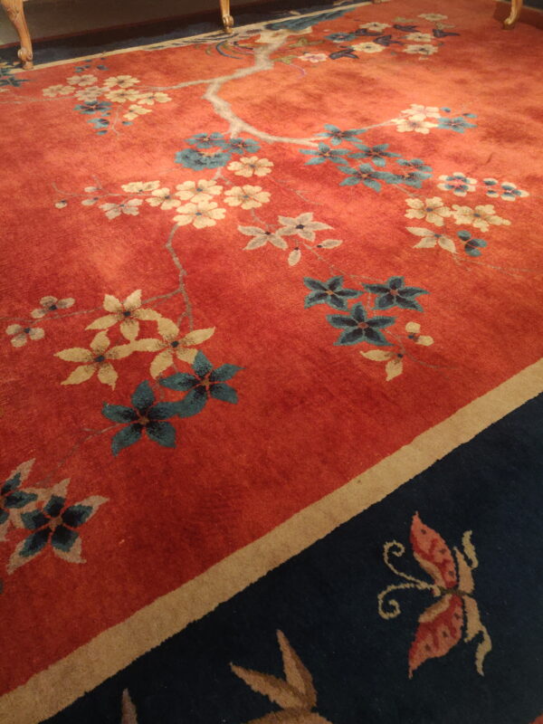 Red floral rug with blue and cream blossoms bordered by dark navy featuring a visible butterfly motif.