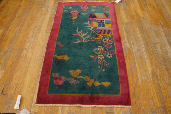 Teal runner rug with a magenta border featuring a pictorial scene of a building and blossoms on wood flooring.