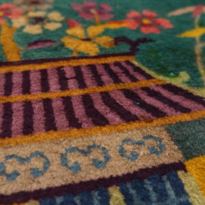 Colorful high-pile rug detail showing a striped pagoda structure, tan base, and flowers on a teal ground.