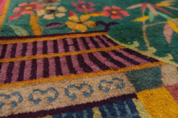 Colorful high-pile rug detail showing a striped pagoda structure, tan base, and flowers on a teal ground.