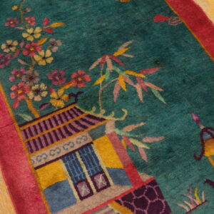 High-pile teal rug with pink border showing detailed floral and pagoda motifs on worn wooden flooring.