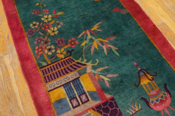 High-pile teal rug with pink border showing detailed floral and pagoda motifs on worn wooden flooring.