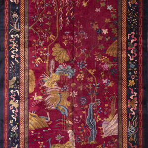 Plush high-pile rug in deep crimson, featuring an ornate floral and avian design with a patterned dark navy border.