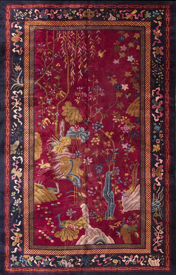 Plush high-pile rug in deep crimson, featuring an ornate floral and avian design with a patterned dark navy border.