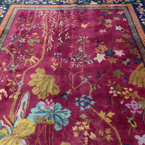 Berry red rug with a lush pile, featuring multicolored botanical motifs and a dark geometric border.