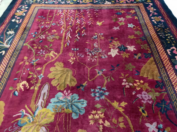 Berry red rug with a lush pile, featuring multicolored botanical motifs and a dark geometric border.