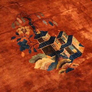 Rust rug detail showing a low pile field with a blue and brown pictorial house and floral motif.