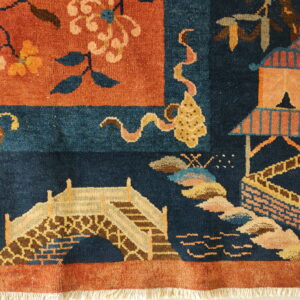 Close-up of a navy and rust high-pile rug with floral, bridge, and pavilion motifs and white fringe.