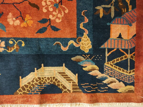 Close-up of a navy and rust high-pile rug with floral, bridge, and pavilion motifs and white fringe.