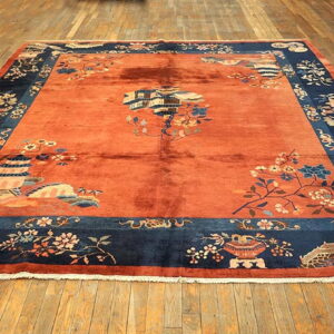Burnt orange rug with a deep blue border, patterned with pagodas, bridges, and flowering branches.