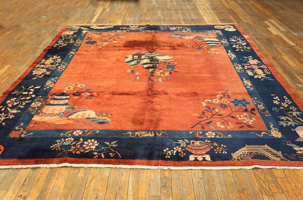 Burnt orange rug with a deep blue border, patterned with pagodas, bridges, and flowering branches.