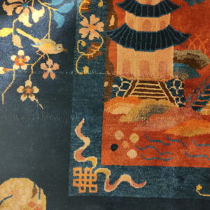 Close-up of a dark blue and rust rug showing floral, bird, and pagoda motifs in bright light.