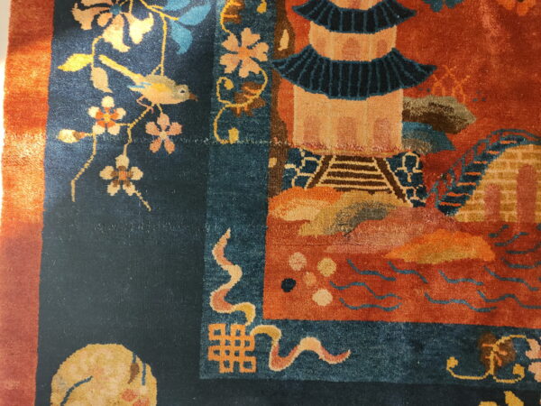 Close-up of a dark blue and rust rug showing floral, bird, and pagoda motifs in bright light.