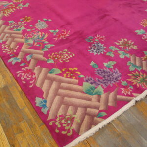 Low-pile fuchsia rug with a latticework border and colorful floral design on wood floorboards.