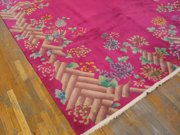 Low-pile fuchsia rug with a latticework border and colorful floral design on wood floorboards.