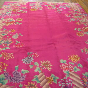 Fuchsia rug featuring a multicolored floral border and geometric basketweave on wood flooring.