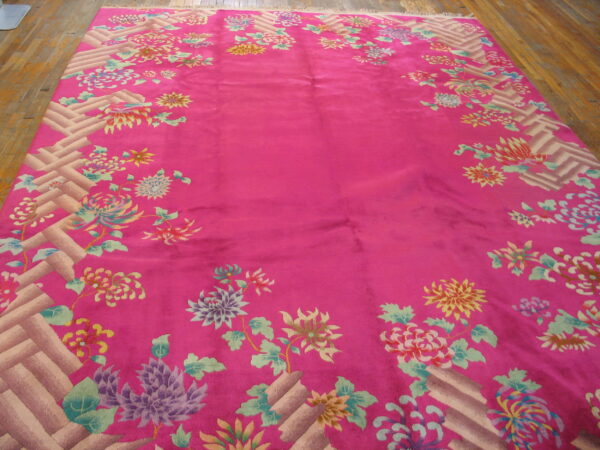 Fuchsia rug featuring a multicolored floral border and geometric basketweave on wood flooring.