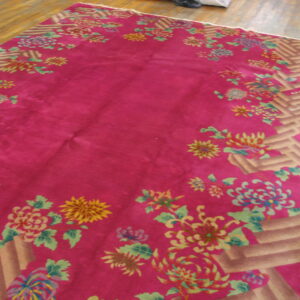Plush magenta rug featuring colorful chrysanthemum floral motifs and a geometric tan border on wood floor.