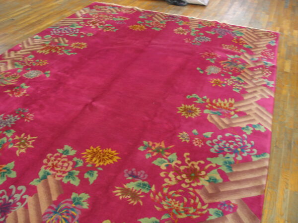 Plush magenta rug featuring colorful chrysanthemum floral motifs and a geometric tan border on wood floor.