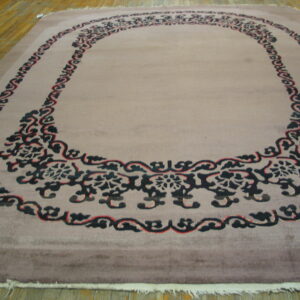 A muted taupe plush rug with a bold black and red floral scroll medallion on a wood floor.